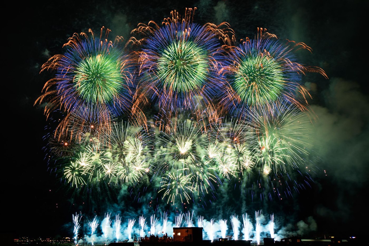 緑や青、金色の花火が夜空に並んで咲く様子